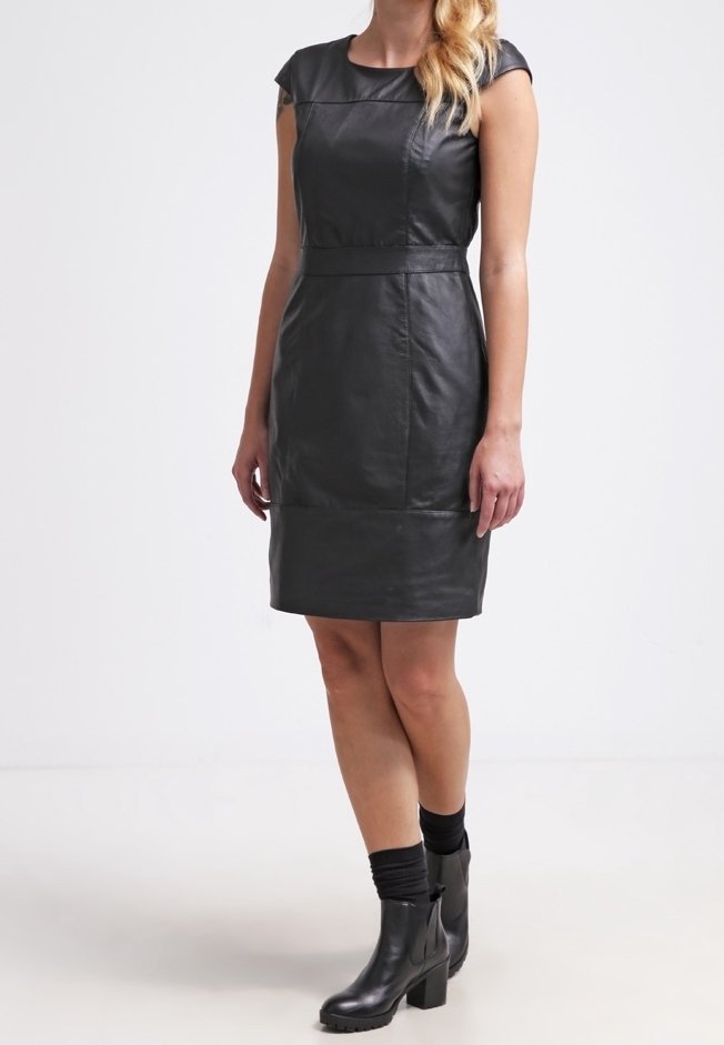 Robe en cuir noir avec manches courtes, coupe ajustée et coutures soulignant la taille. Portée avec des bottines noires et des chaussettes.