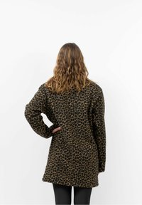 Leopardprint jas in zwart en bruin, gemaakt van een zachte, gestructureerde stof. Heeft een relaxte pasvorm en lange mouwen.