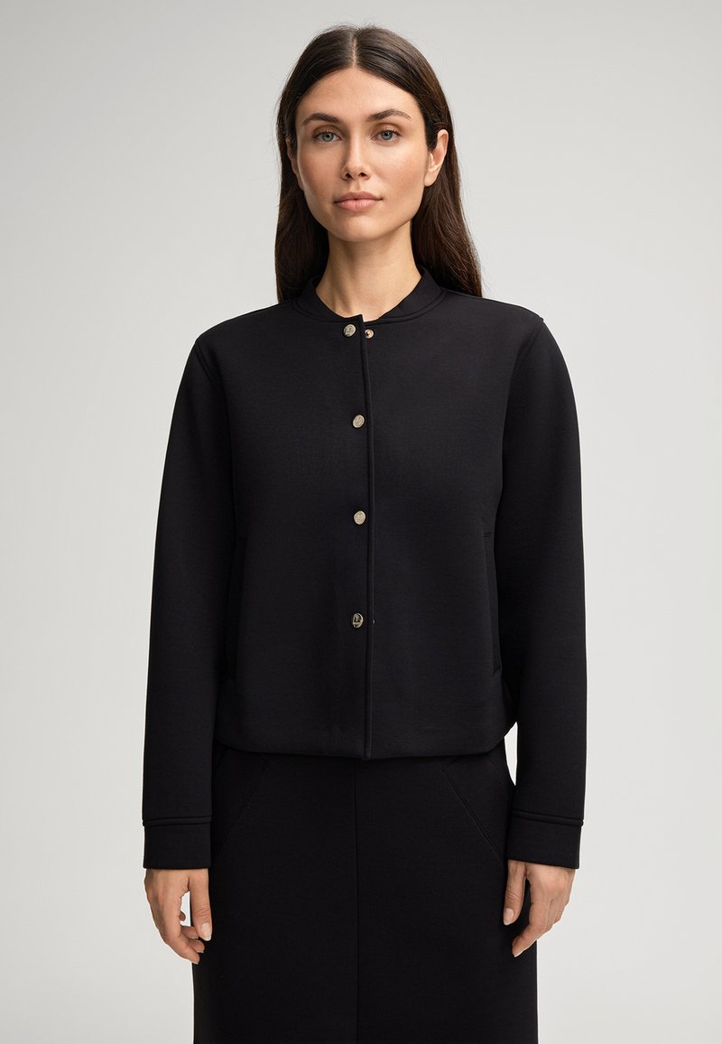 Sweatshirt noir court avec un col rond, des manches longues et des fermetures à boutons métalliques. Tissu lisse avec des poches latérales.