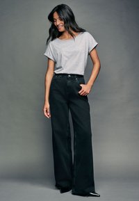 T-shirt en coton gris à manches retroussées, associé à un jean noir taille haute à jambes larges, avec poches et fermeture à boutons sur le devant.