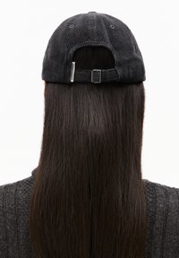 Zwarte corduroy honkbalpet met verstelbare band aan de achterkant, voorzien van een klein label; gezien vanaf de achterkant, met lange donkere haren.