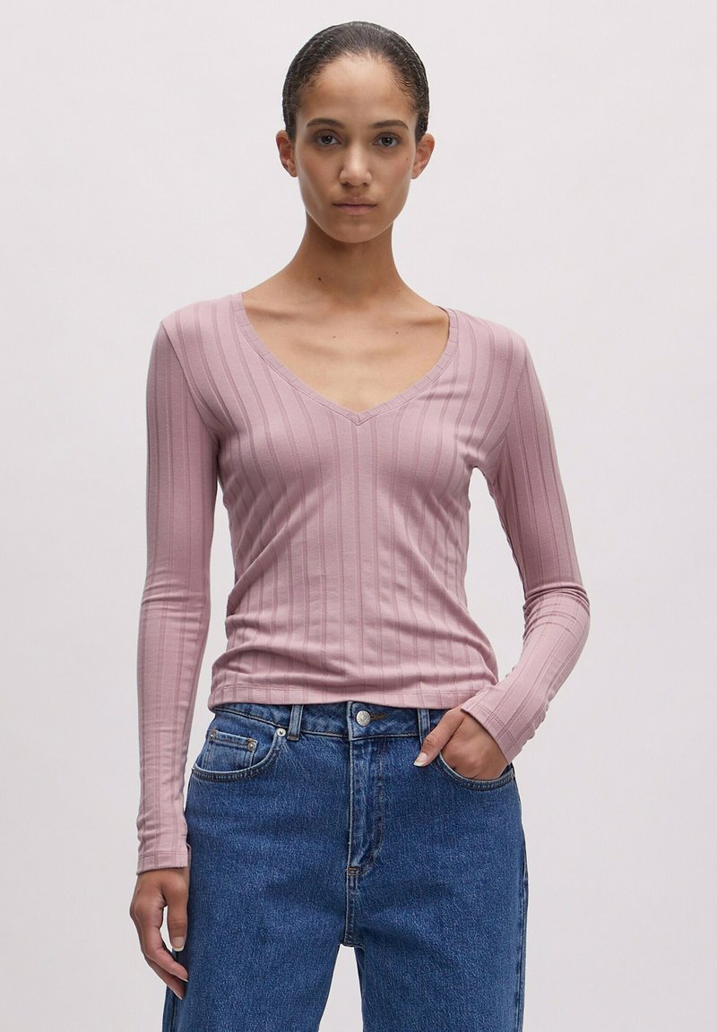 Langärmliges, V-ausschnitt Oberteil aus leicht pinkfarbener Rippstoff, mit einer figurbetonten Form und glatter Textur. Getragen mit blauen, hoch geschnittenen Jeans.