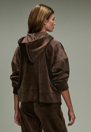 Braune Velours-Hoodie mit lockerer Passform, großer Kapuze und gerippten Bündchen. Strukturierter Stoff und subtiler Glanz verleihen ein weiches Aussehen.