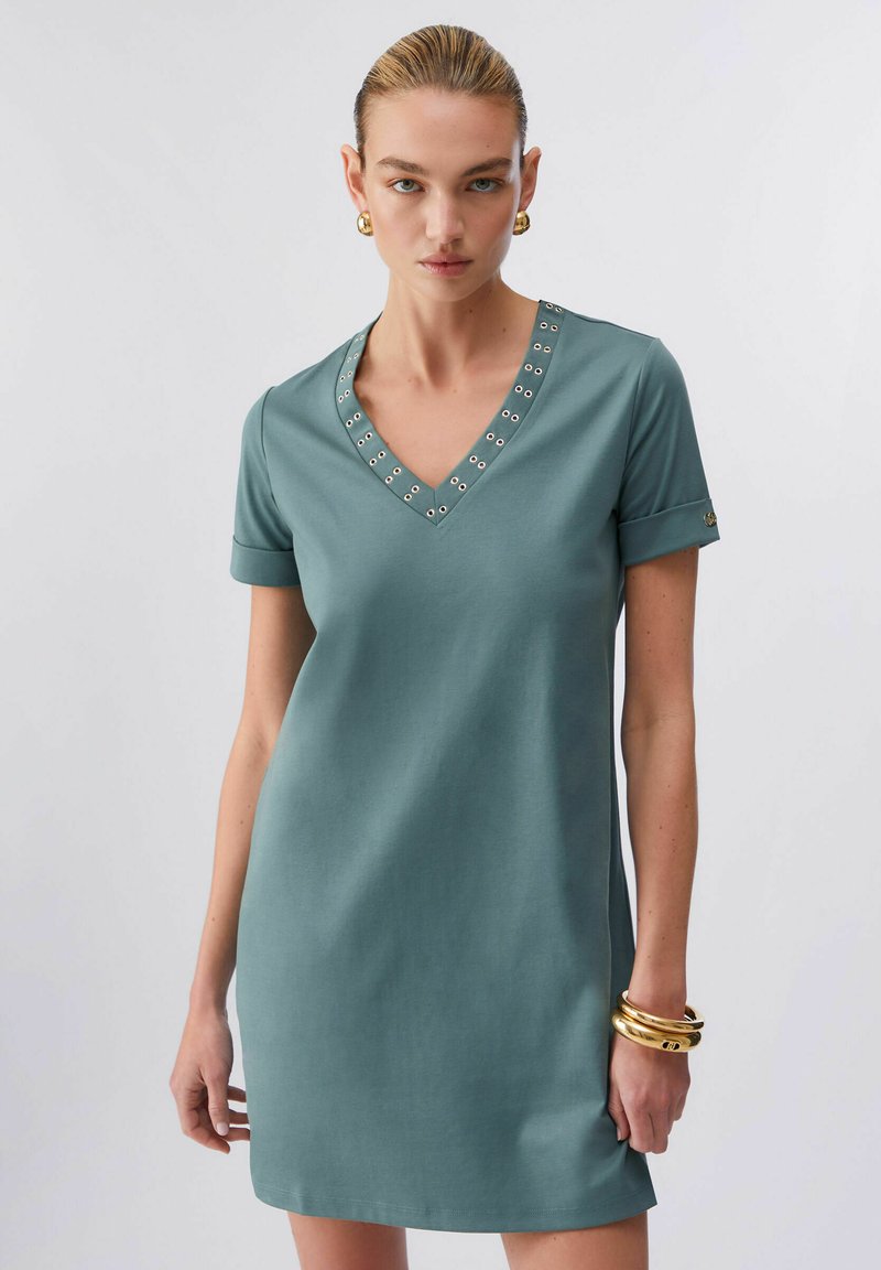 Vestido de manga corta en color verde azulado con escote en V, que presenta ojales metálicos a lo largo del escote y puños remangados. Textura de tela suave.