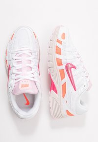 Paire de chaussures de sport blanches avec des accents roses et orange, y compris les logos Nike roses, vues de haut et de côté sur un fond blanc.