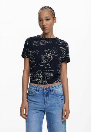 T-shirt nera a maniche corte con disegni in bianco di un personaggio dei cartoni animati e testo. Abbinata a jeans azzurri chiari decorati con piccoli punti.