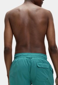 Turkusowe szorty kąpielowe z elastycznym pasem, z tylną kieszenią i gładkim, lekkim materiałem. Brak widocznych wzorów lub ozdób.