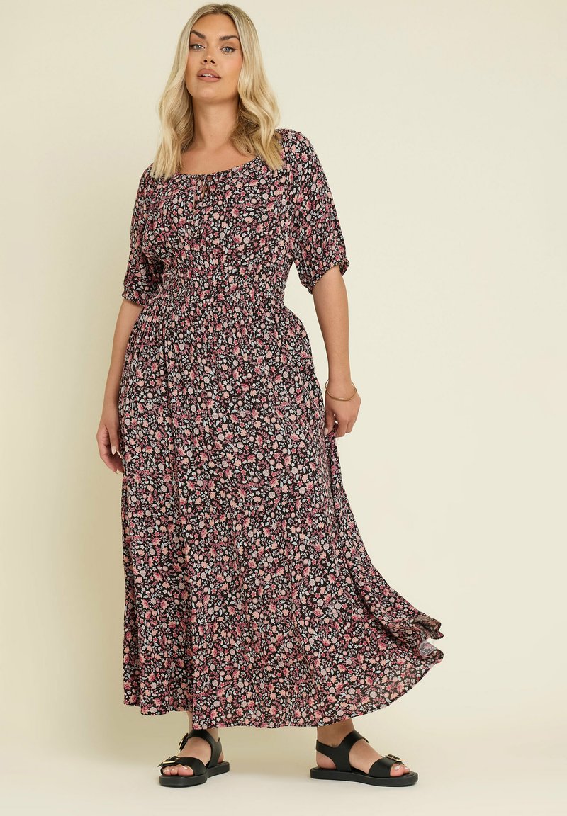 Blommig maxiklänning med svart bakgrund och rosa och vita blommor, korta ärmar, en samlad midja och en fladdrande nederkant.