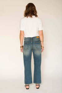 Jean taille haute à jambes larges en denim bleu moyen avec effet délavé, design à cinq poches, et une pièce en cuir marron clair sur la ceinture arrière.