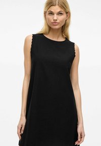 Robe noire sans manches avec un col rond et des bords scallopés aux épaules. Fabriquée dans un tissu léger et texturé avec une coupe ample.