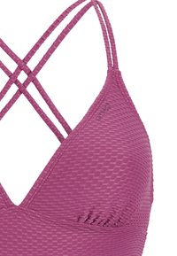 Różowy sportowy biustonosz z trójkątnymi miseczkami i podwójnymi, krzyżującymi się ramiączkami, wykonany z tkaniny o wzorze waflowym.
