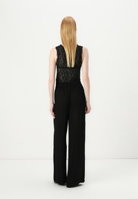Mono negro con parte superior de encaje y diseño de pierna ancha, que presenta una cintura ceñida y tela texturizada, visto desde la parte posterior.