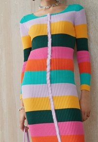 Vestido de punto acanalado con rayas horizontales multicolores en teal, amarillo, verde, rosa y púrpura, con un cierre de botones en la parte delantera y mangas largas.
