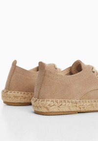 Beige suede shoes with a low profile, featuring a braided jute sole and visible stitching on the upper, designed for casual wear.