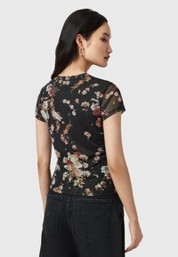 T-shirt nera con stampa floreale, maniche corte, caratterizzata da una texture trasparente e vari motivi floreali colorati su uno sfondo scuro.