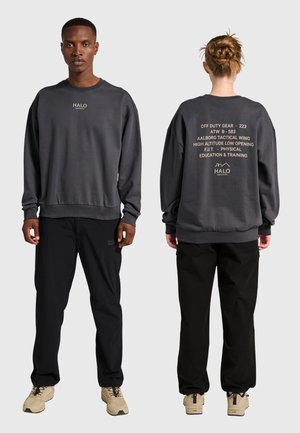 Vorder- und Rückansicht von zwei Personen, die dunkelgraue Sweatshirts mit Textlogos und schwarze Hosen tragen, stehend vor einem schlichten hellgrauen Hintergrund.