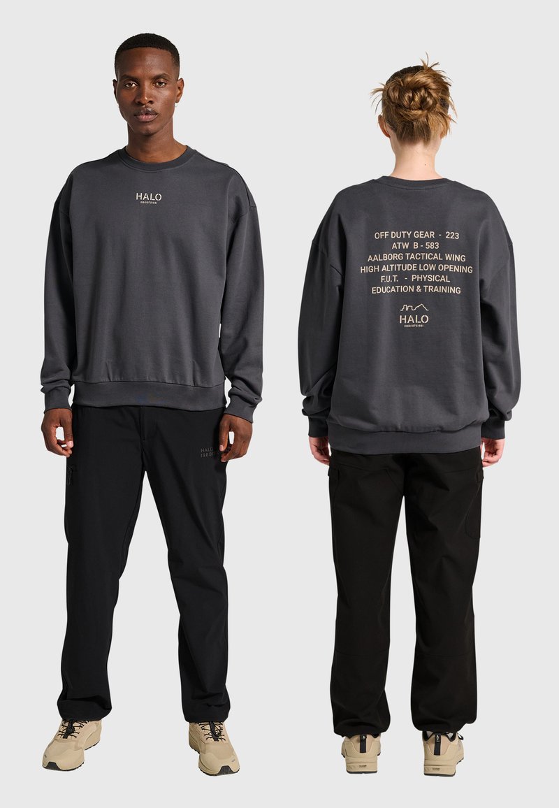 Voor- en achterkant van twee personen die donkergrijze sweatshirts met tekstlogo's en zwarte broeken dragen, staand op een effen lichtgrijze achtergrond.