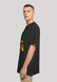 Schwarzes Kurzarm-T-Shirt aus Baumwollstoff mit einem Grafikdesign, das grüne, gelbe und schwarze Abschnitte zeigt, die Gesichter darstellen.