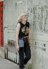 Un haut débardeur noir court arborant un logo Harley-Davidson, un jean noir taille haute et un petit sac bandoulière bleu sur un fond patiné.
