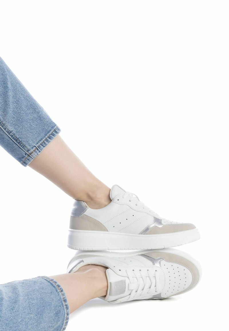 Zapatillas deportivas blancas con acentos en gris y plateado, parte superior de cuero suave, punta redonda, detalles perforados y una suela gruesa blanca.