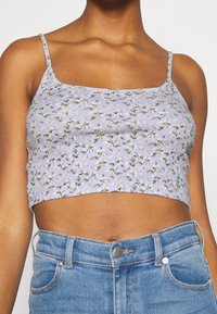 Blommig crop top i ljuslila ribbat tyg, med tunna axelband, små vita och gula blommönster, samt en figursydd design.