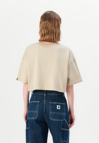 Beige t-skjorte med kort erme, kombinert med mørkeblå denim cargo-bukser med flere lommer og en etikett bak.