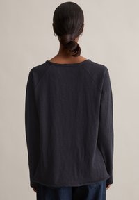 Ciemnoszary, długi rękaw z luźnym krojem, rękawy raglanowe i surowa krawędź przy dekolcie. Miękka, teksturowana tkanina z lekko zaokrąglonym dołem.