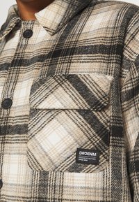 Rutigt flanellskjorta i beige, svart och vitt. Har en bröstficka, knappstängning och DRDENIM-logotyp. Mjuk, strukturerad tyg.