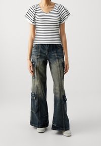 Top de rayas, de manga corta y canalé en blanco y negro, combinado con pantalones cargo de mezclilla desgastados y holgados, que presentan grandes bolsillos y un acabado desteñido.