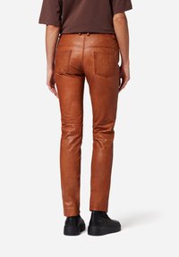 Bruine leren broek met een strakke pasvorm, twee achterzakken en subtiele textuur. Gecombineerd met zwarte instap schoenen voor contrast.