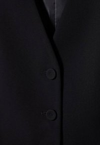 Czarna, dopasowana kamizelka wykonana z gładkiej tkaniny, posiadająca dekolt w kształcie litery V, dwa czarne guziki oraz smukły, wyprofilowany krój.