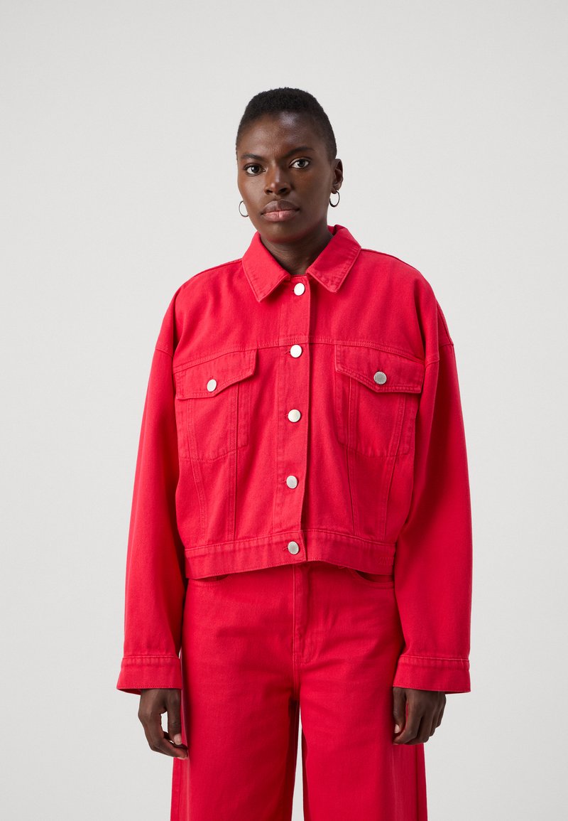 Rød denimjakke med cropped design, frontlommer og sølvknapper, sammen med matchende røde bukser. Glatt tekstur, uformell stil.