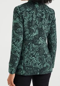 Mörkgrön kavaj med ett tryck av löv i ljusare grönt. Har lång ärm och en figursydd design, tillverkad av texturerad tyg.