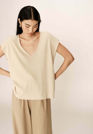 Haut en tricot beige côtelé avec un col en V, des manches courtes et une coupe décontractée, associé à un pantalon léger beige ample, mettant en valeur un tissu doux et texturé.