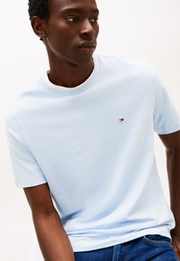 Šviesiai mėlynas medvilninis marškinėlių su trumpomis rankovėmis ir apvalia kaklo linija, kairėje krūtinės pusėje yra mažas logotipas ir lygus paviršius.