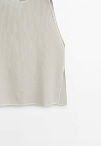 Haut sans manches en maille de couleur crème avec un col rond et une fente sur le côté sur fond blanc.