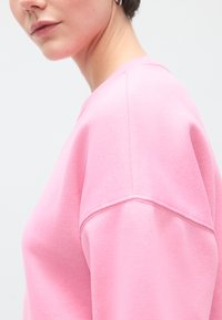 Ροζ φούτερ με απαλή υφή, με στρογγυλή λαιμόκοψη και ραφές ώμων που πέφτουν για άνετη εφαρμογή.