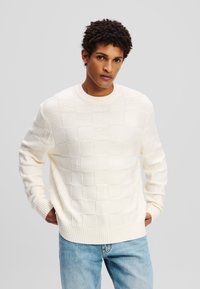 Strickpullover in Creme mit einem Rautenmuster und erhöhten Akzenten, gerippten Bündchen und Saum, runder Halslinie und lässiger Passform.