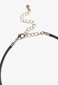 Șnur împletit negru cu accesorii din aur, prevăzut cu un cârlig tip homar și o extensie de lanț cu linkuri circulare. Accente texturate și metalice.