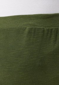Žalias ribotas audinys su lygia tekstūra ir elastinga juosta. Dizainas turi šoninio kišenės detalę.