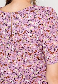 Purple floral top featuring short sleeves, keyhole back detail, and gathered fabric around the waist with patterns in pink, white, and black.