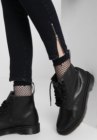 Botas de combate de cuero negro con cordones, parte superior texturizada y suela de goma. Combinadas con jeans oscuros que cuentan con un zipper lateral y medias de red.