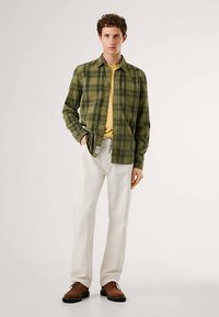 Žaliai geltonas languotas marškinys dėvimas ant geltonos marškinėlių, derinamas su baltais kelnėmis ir rudais batais. Kasdienis, laisvo kirpimo.