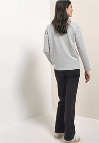 Szary longsleeve z luźnym krojem, w połączeniu z czarnymi spodniami i jasnymi trampkami. Gładka tekstura, prosty design.