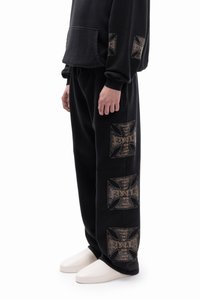 Black sweatpants with gold graphic prints on the side, featuring a relaxed fit and soft texture. The design includes distinct patterns.