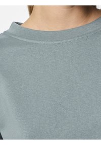 Gros plan sur une personne portant un t-shirt uni gris clair à col rond, mettant l'accent sur l'encolure et la partie supérieure de la poitrine.