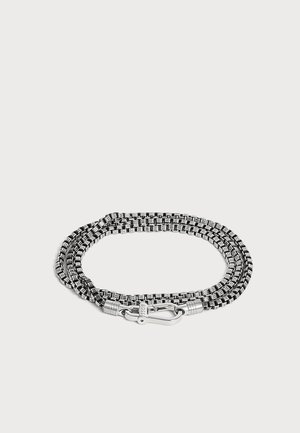 Bracelet en corde tissée noir et blanc avec fermoir en métal argenté sur fond clair.