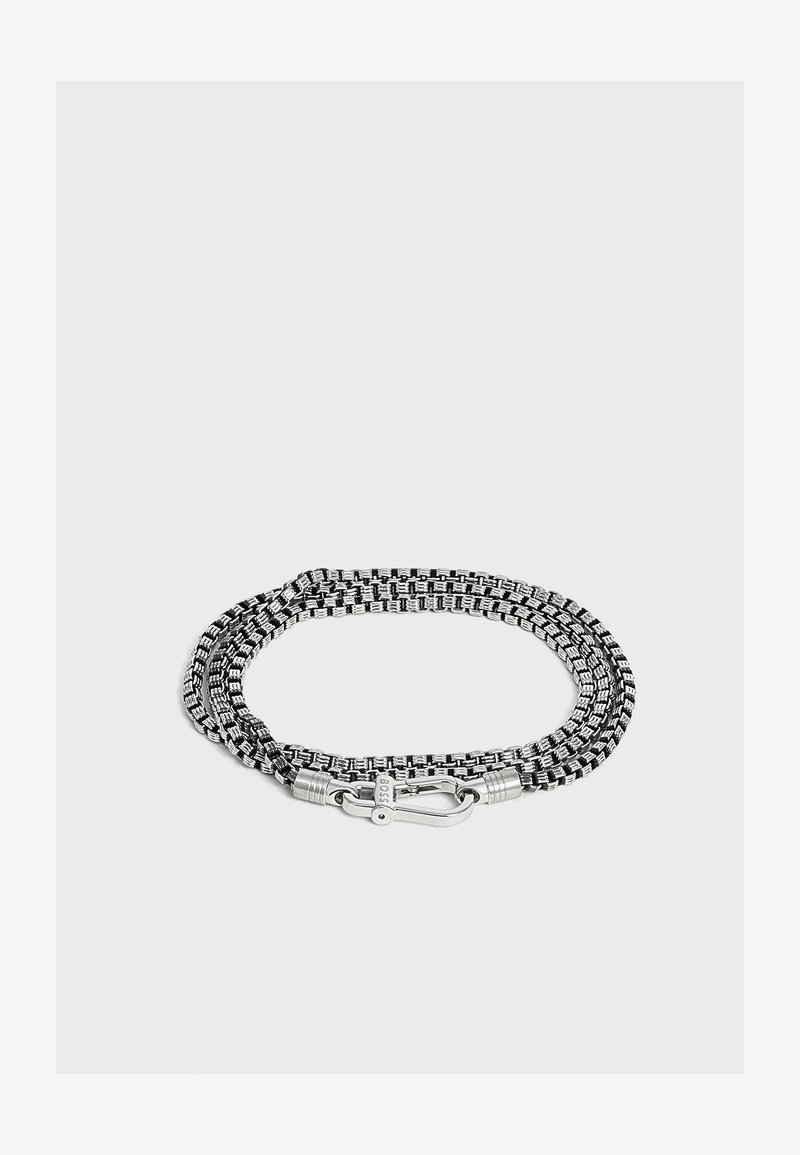 Bracelet en corde tissée noir et blanc avec fermoir en métal argenté sur fond clair.
