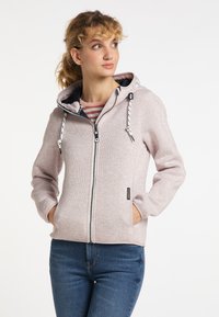 Hoodie rosa chiaro con zip, realizzato in tessuto morbido, dotato di cappuccio, chiusura con zip anteriore e dettagli con coulisse; abbinato a jeans blu.