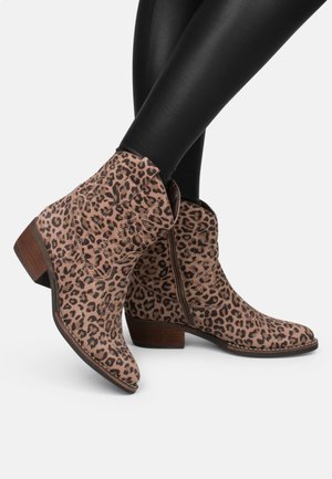 Bottines en daim doux, couleur fauve avec un imprimé léopard, dotées d'un talon en bois empilé. Fermeture éclair sur le côté et détails de couture décorative sur les côtés.